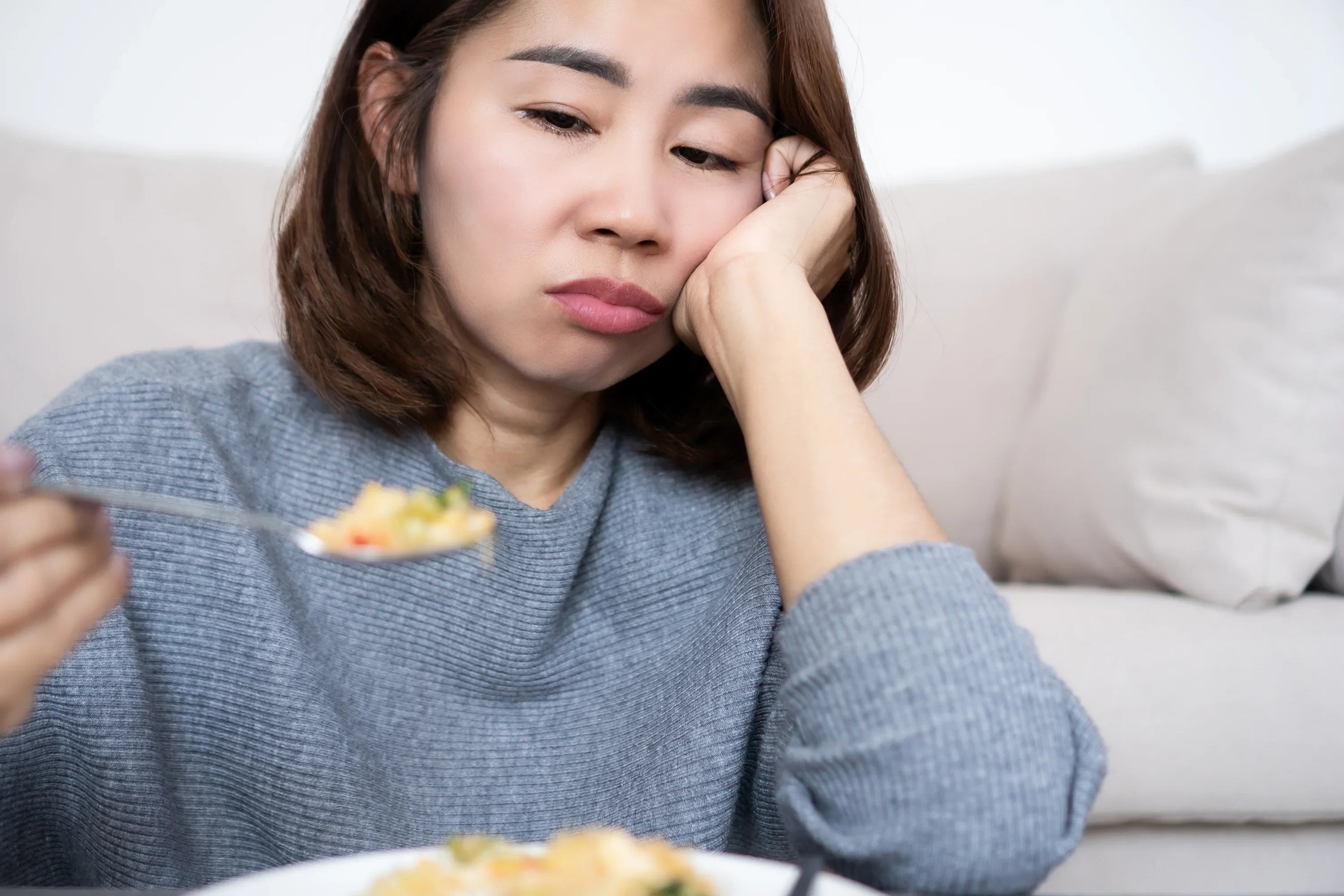 Woman sitting on a couch with a plate of food, looking uninterested.